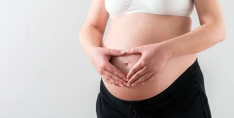 Hands folded in the shape of a heart on the middle of the belly of a pregnant Stock Photos