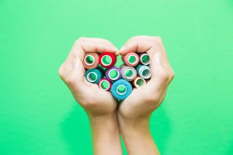 Hands folded in the shape of a heart with spools of thread. Stock Photos
