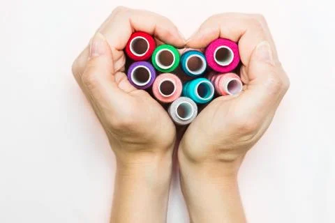 Hands folded in the shape of a heart with spools of thread. Stock Photos