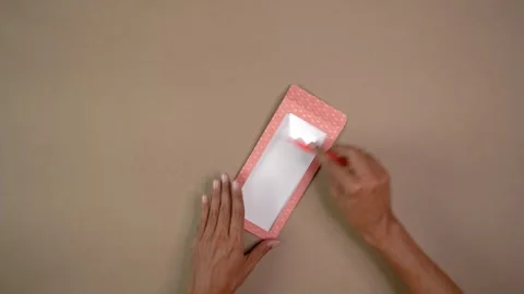 Hands Folding and Creasing Patterned Cardstock with Tool on Neutral Tabletop Stock Footage 345617132