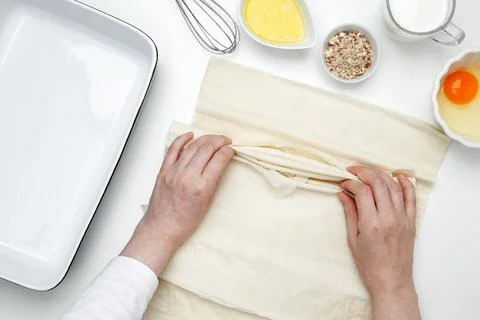 Hands folding phyllo dough with egg, butter, nuts, and milk for baking Crinkl Stock Photos