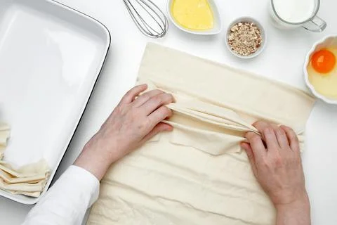 Hands folding phyllo dough with egg, butter, nuts, and milk for baking Crinkl Stock Photos