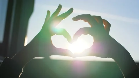 Hands forming a heart in front of a window during romantic sunset. Stock Footage 145428169