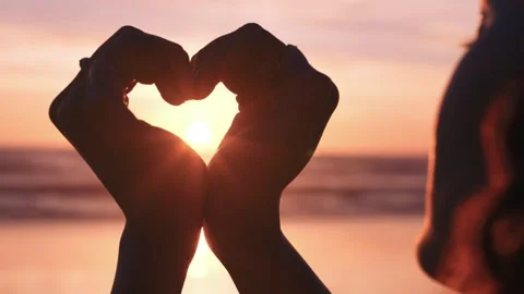 Hands forming heart shape framing golden sunset over ocean waves during Stock Footage 340880751
