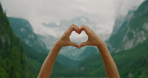 Hands forming a heart shape, framing mountain peaks and a misty sky in the Stock Footage 342464264