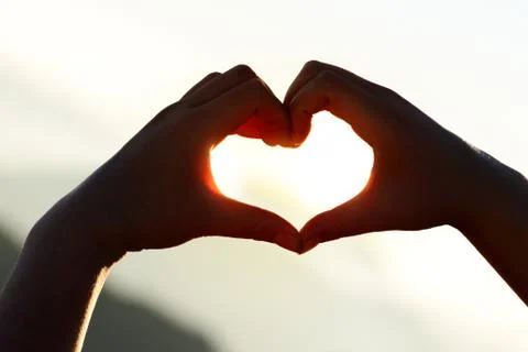 Hands forming a heart shape at sunset with mountains background. Foto stock