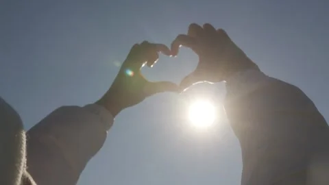 Hands Forming a Heart Shape Towards the Sun in a Clear Sky Stock Footage 293596003