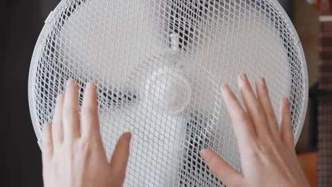 Hands in Front of Spinning Electric Fan Indoors Showing Airflow and Cooling Stock Footage 345690233