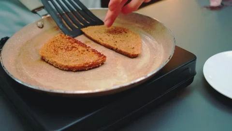 Hands frying two slices of bread in a speckled pan on electric cooktop 库存影片 342863697