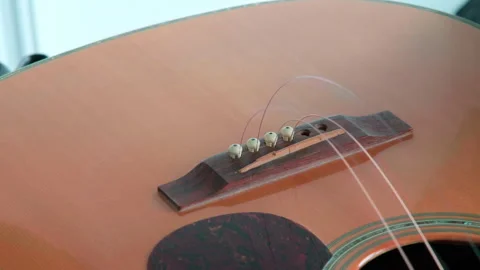 Hands gently fitting three base strings and bridge pins on acoustic guitar Stock Footage 344742287