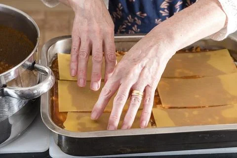 Hands gently place lasagna sheets over a creamy sauce Stock Photos