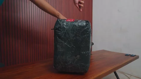 Hands Gently Placing a Dark Wrapped Delivery Package on a Wooden Table Stock Footage 333319765