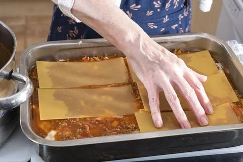 Hands gently press cheese sheets over rich sauce Stock Photos