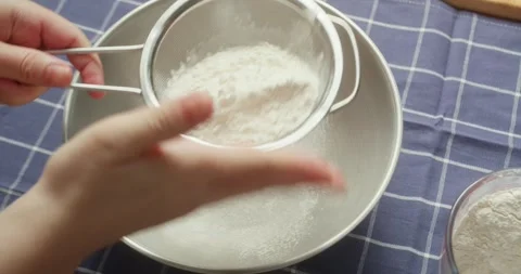 Hands gently sifting flour through a metal sieve in a home kitchen, baking Stock Footage 325729666