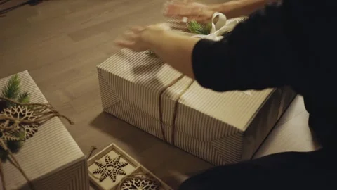 Hands Gently Smooth and Adjust a Christmas Gift Wrapped in Striped Paper - Stock Footage 332684150