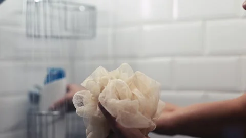 Hands gently squeezing a soft shower loofah under running water, showcasing the Stock Footage 323372359