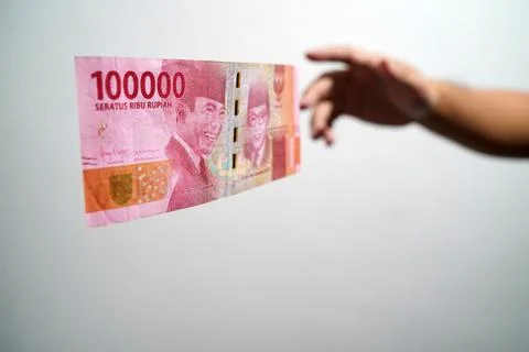 Hands getting ready to catch a hundred thousand rupiah bill on a white backgr Stock Photos