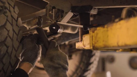Hands in gloves and work clothes are repairing a spare part of a car in a garage Stock Footage 129843347