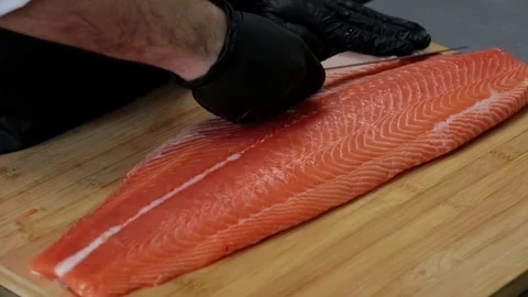 Hands with gloves cut red salmon with a knife on a wooden board Stock Footage 127203504