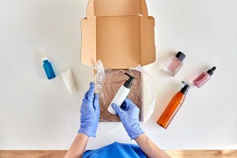 Hands in gloves packing parcel box with cosmetics Stockfoto's