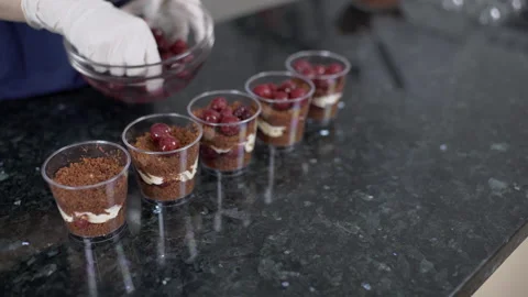 Hands in gloves put cherry in a chocolate dessert on the kitchen table. Stock Footage 87135435