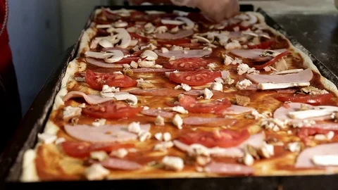 Hands in gloves put chopped mushrooms on the surface of a large square pizza Stock Footage 92634423