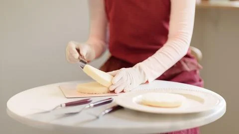 Hands in gloves using cake leveler to slice sponge layer on white table for.. Stock Photos