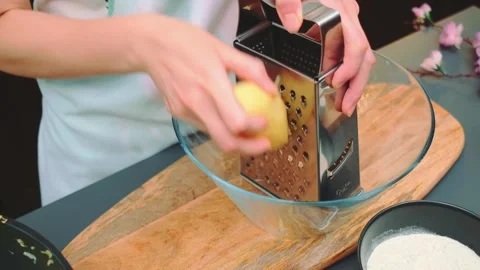 Hands grating raw yellow potato over glass bowl in kitchen Видео 342889224