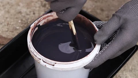 Hands in gray protective gloves stir dark varnish with wooden sticks Video stock 334135937