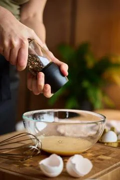 Hands grinding pepper into egg mixture in glass bowl on kitchen counter Foto stock