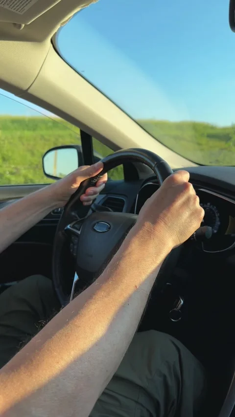 Hands gripping steering wheel while driving through summer nature. Driver n.. Stock Footage 340144630