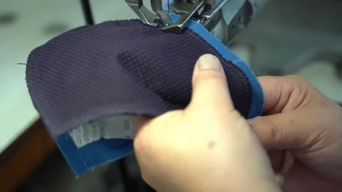Hands guide a curved indigo fabric panel through an industrial sewing machine Stock Footage 346797335