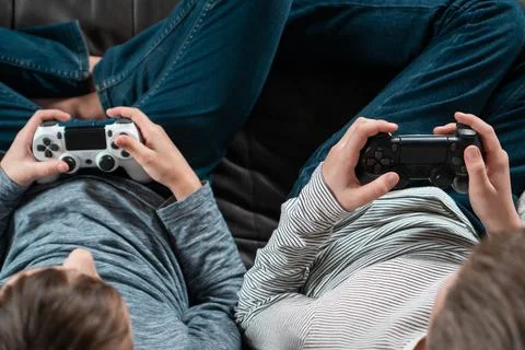Hands of guys sitting on sofa with game joysticks, from above view. Kids in Stock Photos