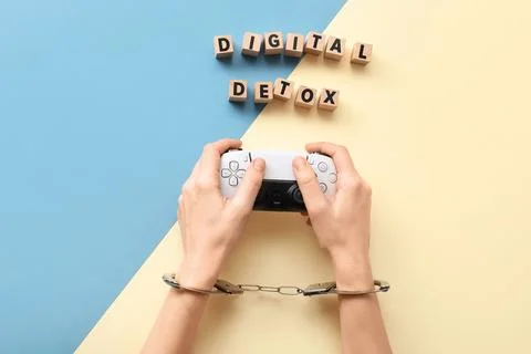Hands in handcuffs holding a game controller with "digital detox" text on woo Stock Photos