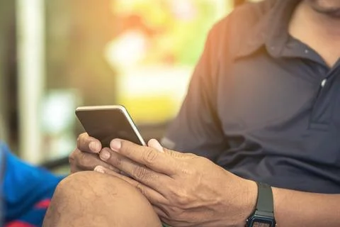 Hands of happy man using cell phone sitting on couch at home. View of man l.. 스톡 사진