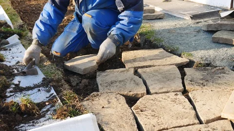 Hands hits a stone with a hammer to make it fit and to place stone pavers Stock Footage 129232826