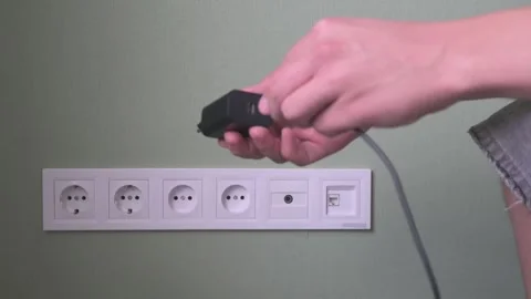 Hands hold a black electrical plug, preparing to connect or disconnect Stock Footage 317605731