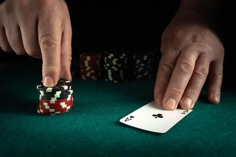 Hands hold a card and stack of poker chips on a green table. The player prepa Foto stock