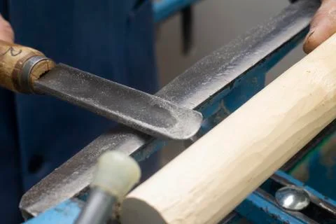 Hands hold a chisel for processing on the turning machine of a wooden bar Stock Photos