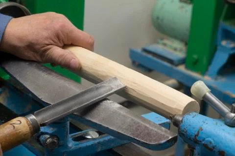 Hands hold a chisel for processing on the turning machine of a wooden bar Stock Photos