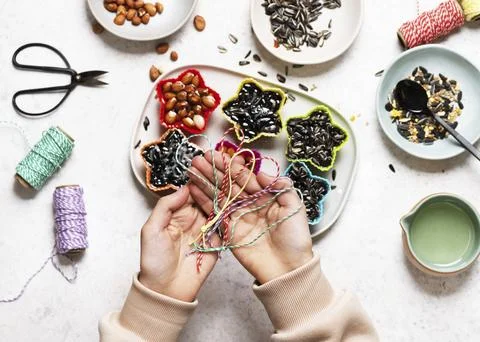 Hands hold colourful threads in front of bowls with seeds. String is inserted Foto stock