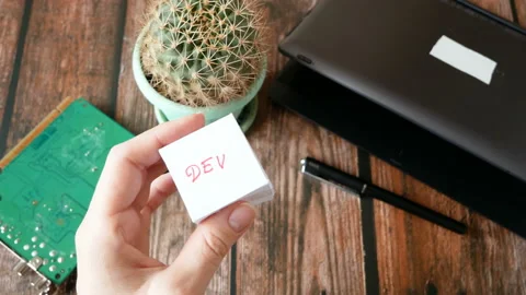 Hands hold cubes with Dev and Ops words near laptop and motherboard. DevOps  Stock Footage 123996060