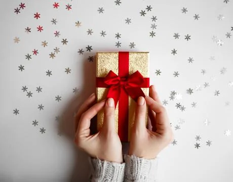 Hands hold a gift on a white background with silver snowflakes Stock Photos