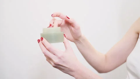 Hands hold a green jar with a white lid of skincare product in a bright room at Stock Footage 331542360