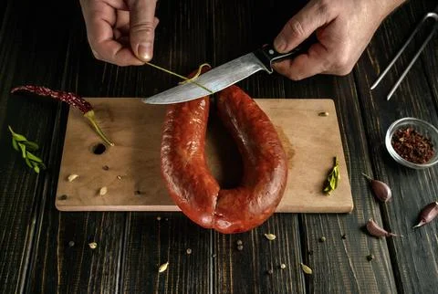 Hands hold a knife as it cuts a string tied around a sausage on a wooden boar Stock Photos
