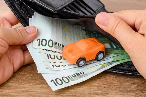 Hands hold an open black leather wallet with 100 euro banknotes and toy car Stock Photos