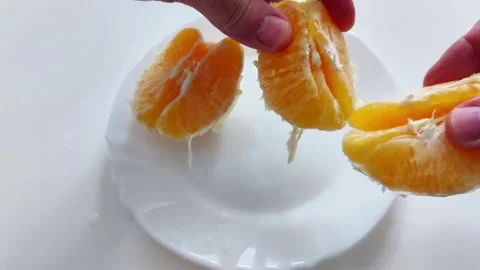 Hands Hold Peeled Orange Segments Above White Plate on Clean Surface Video stock 329543271