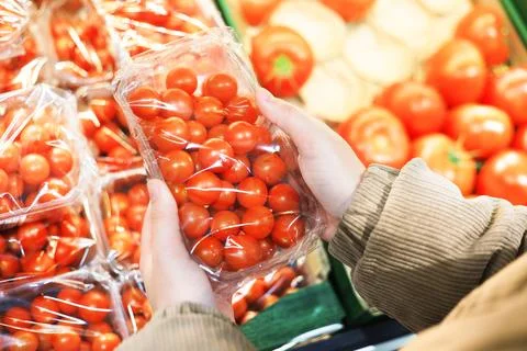 Hands hold a plastic container of bright red cherry tomatoes in a supermark.. 스톡 사진
