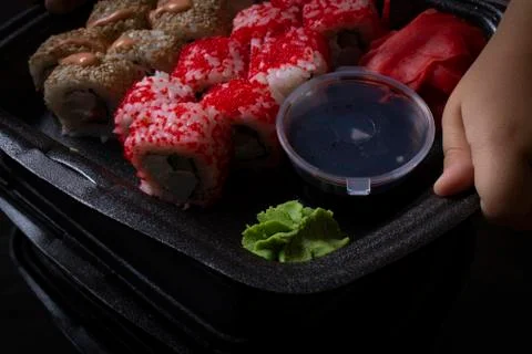 Hands hold set of red and yellow sushi rolls. Dark mood photo Stock Photos