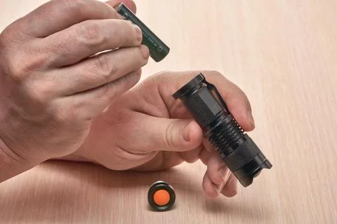 Hands hold a small black flashlight and replace the battery in it Stock Photos
